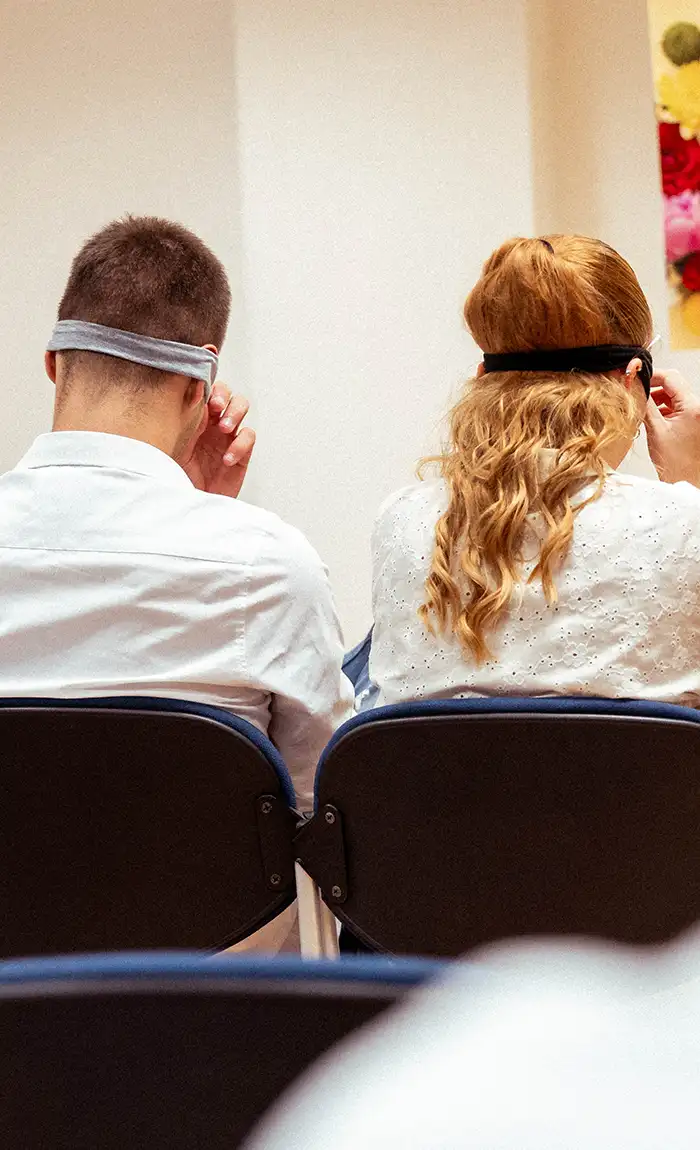 Dvije osobe sjede u publici s povezima preko očiju tijekom događanja.
